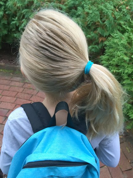 Young blond girl wearing a side ponytail and a blue backpack.