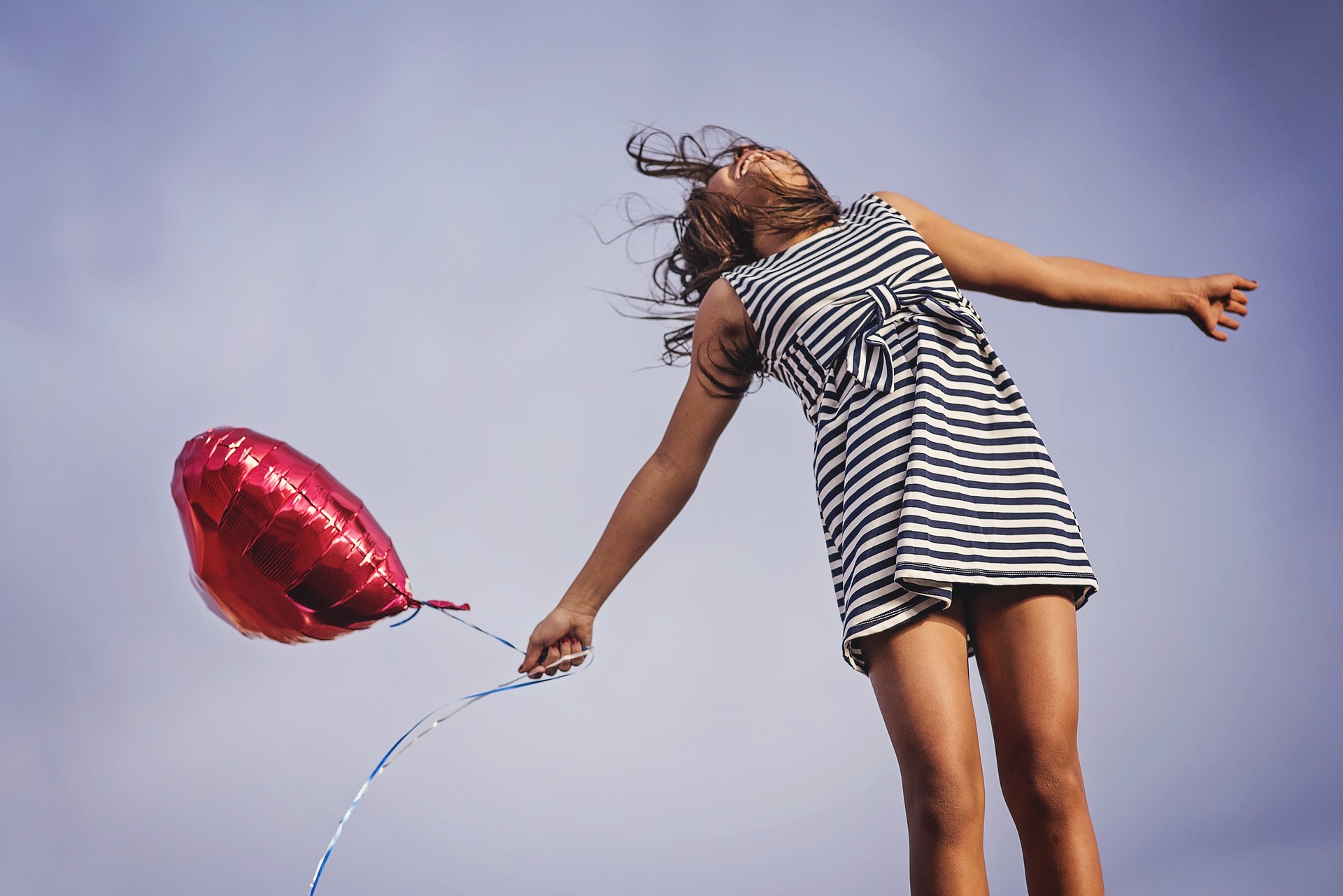 Young girl in a dress jumping with a balloon.