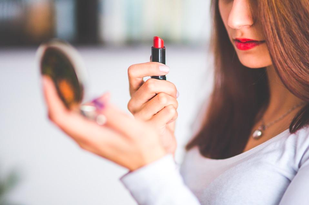 Woman putting on her lipstick while looking in a small mirror.