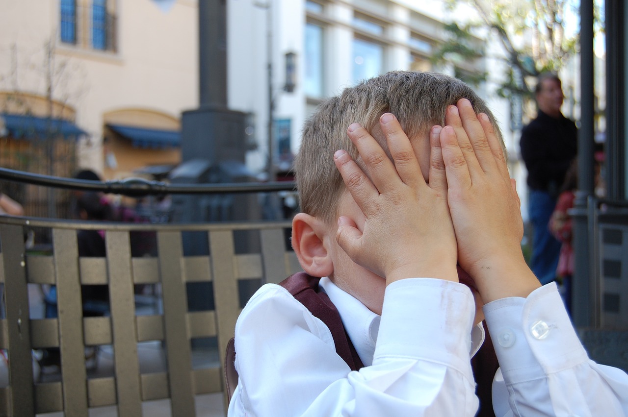 Young boy with his hands over his face.