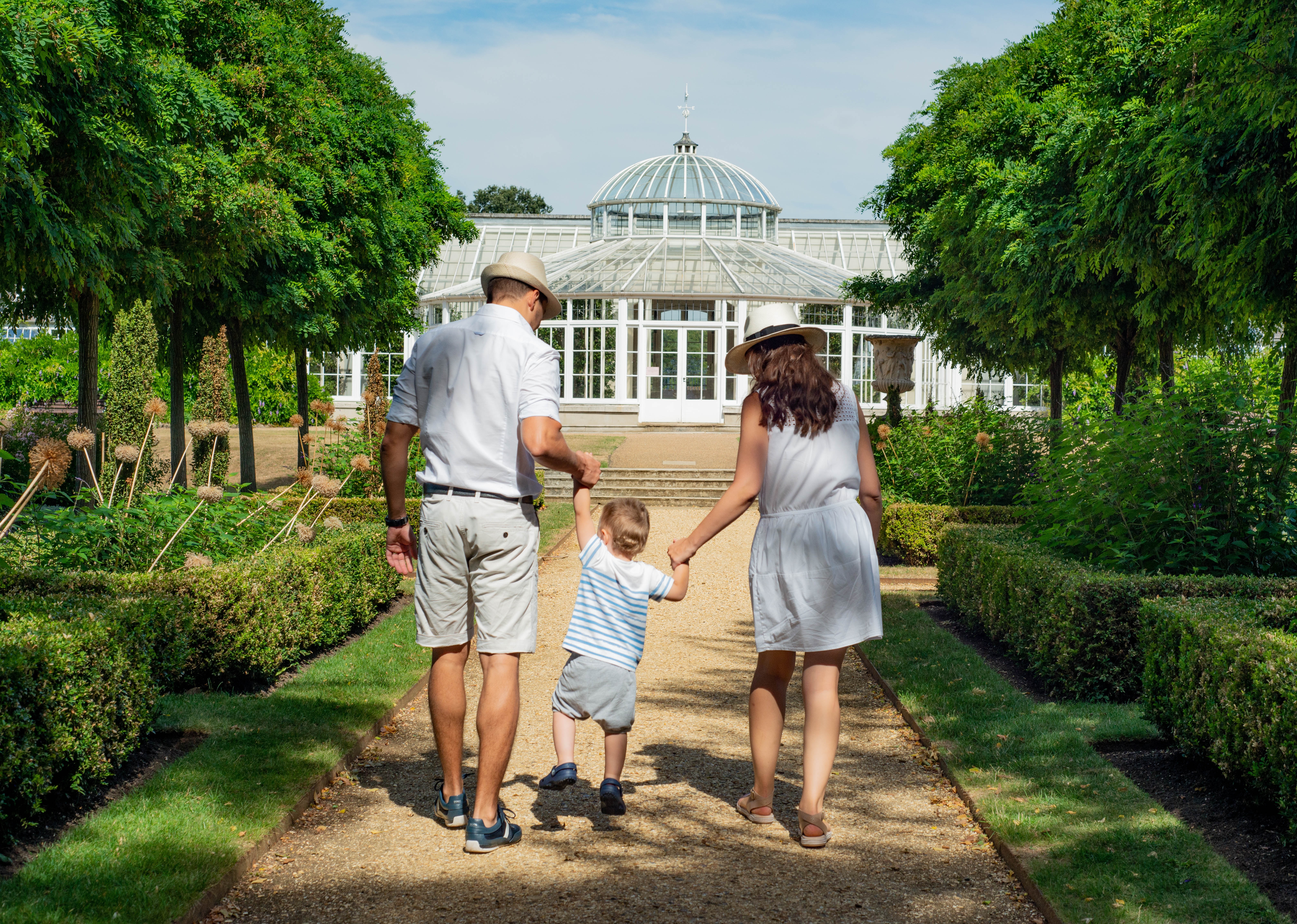 Family with a mom, dad, and child walking along a paved walkway to an arboretum.