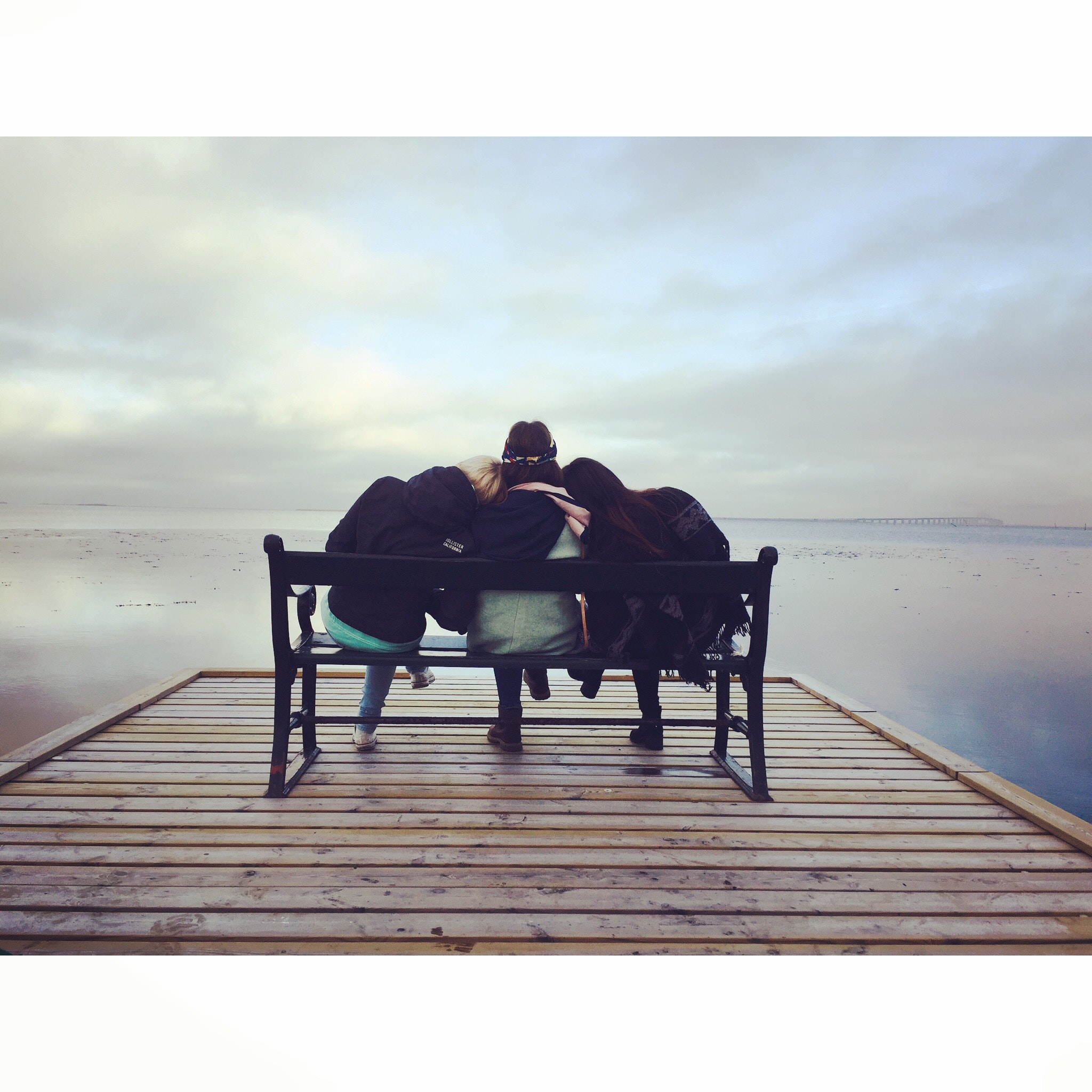 Friends sitting on a bench on a dock overlooking a lake.