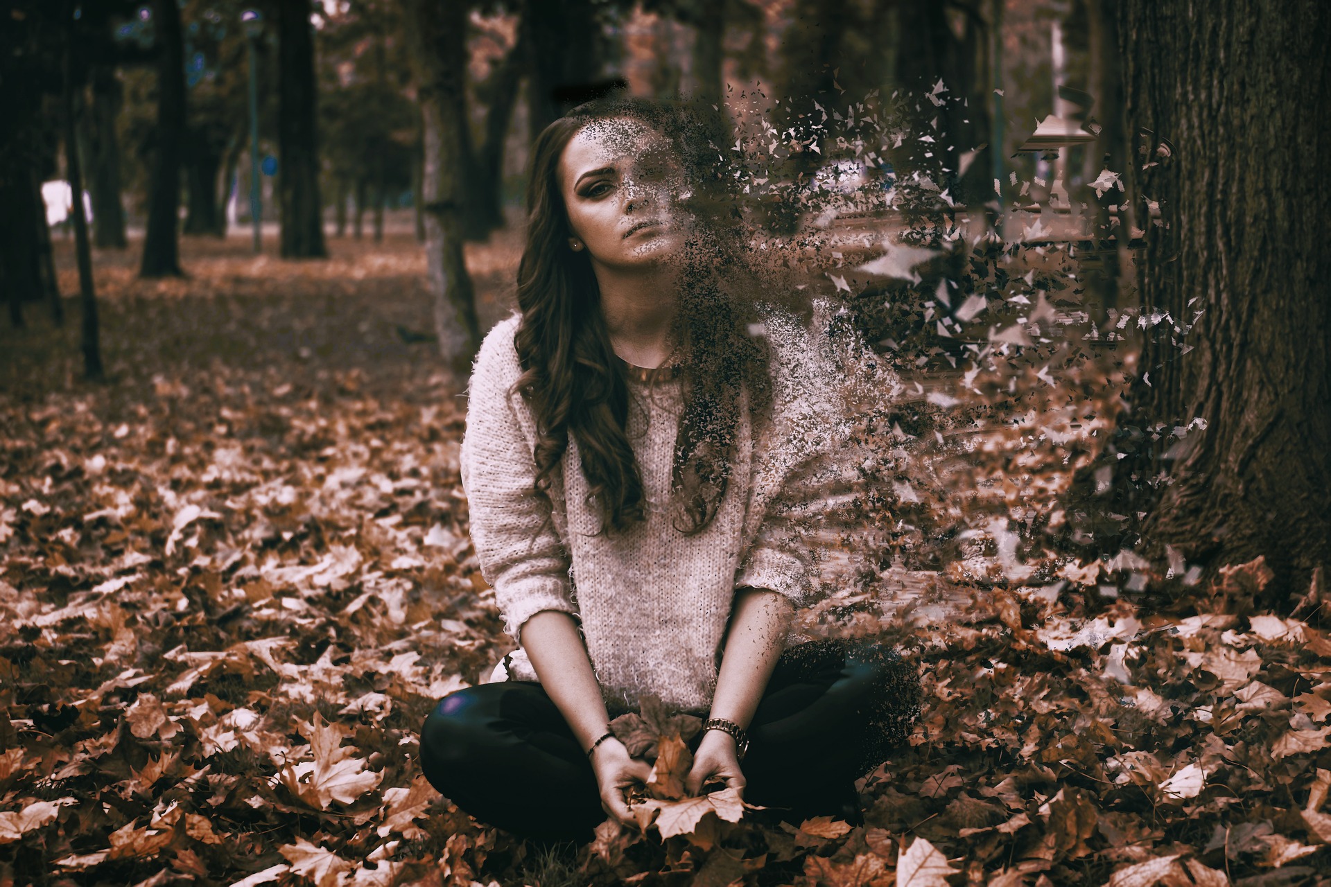 Woman sitting on leaves, looking sad, depicting depression.