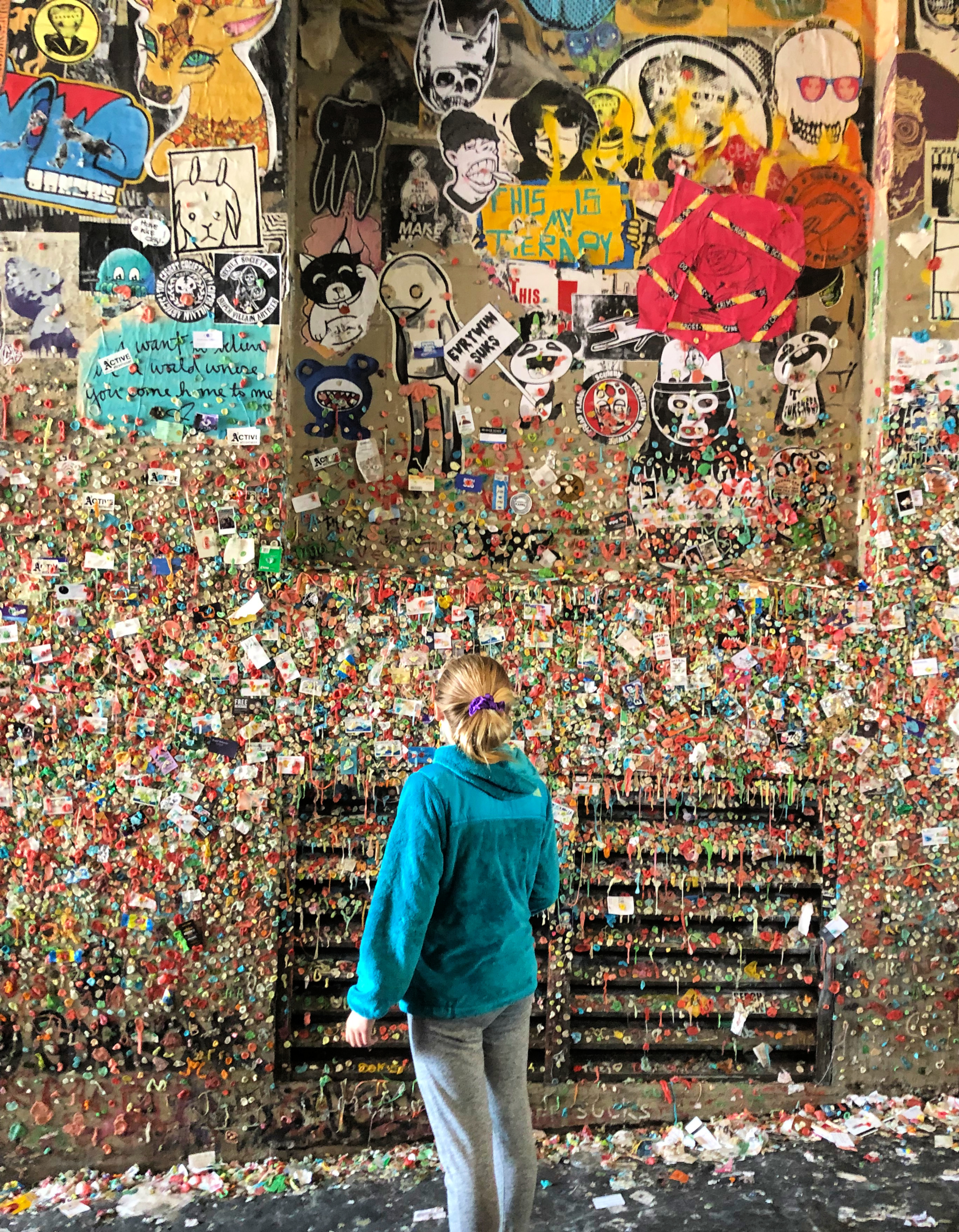 Girl looking at the gum covering the walls of an alley at the Seattle Gum wall.