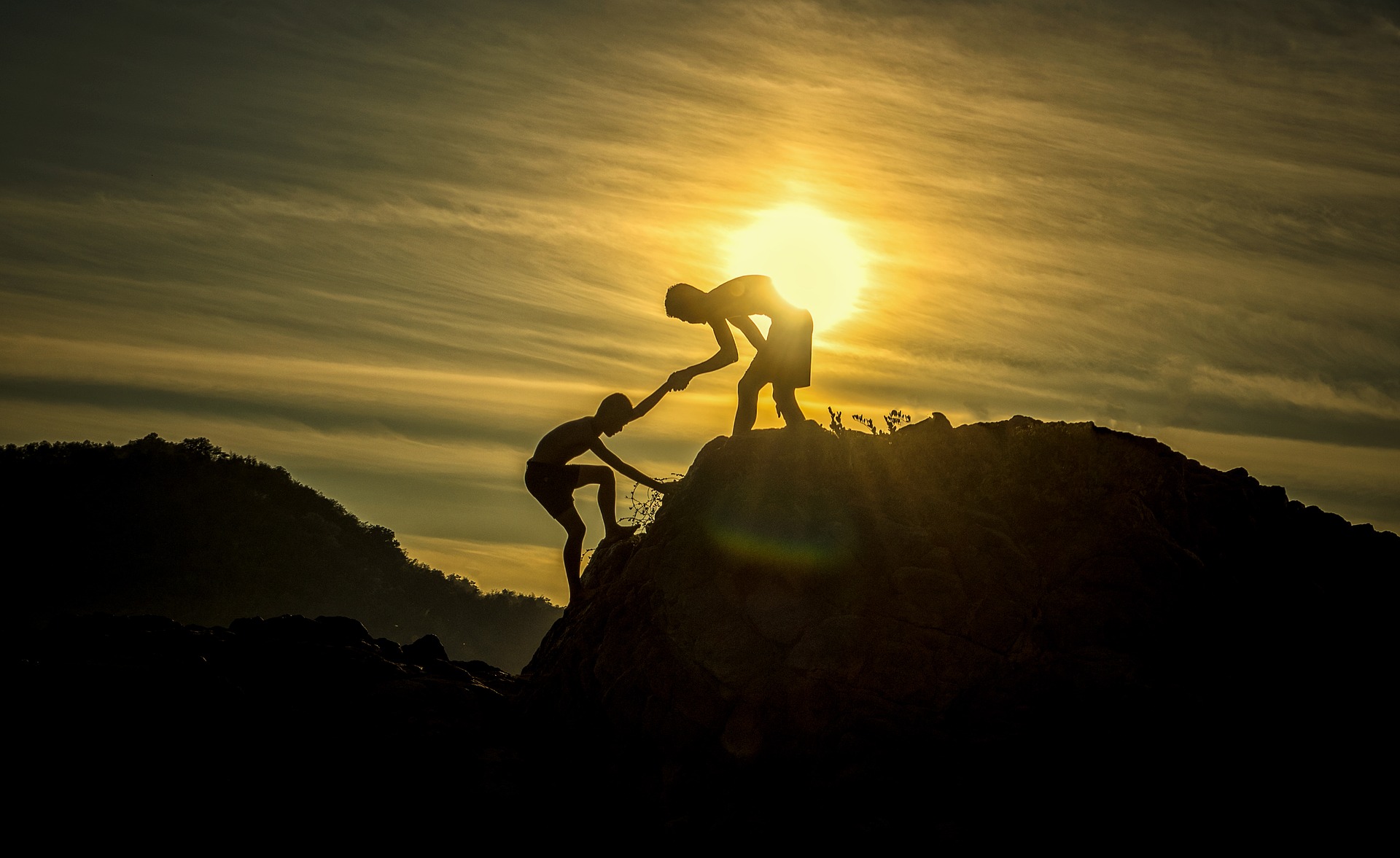 Person helping pull up another person while they are hiking during a sunset.