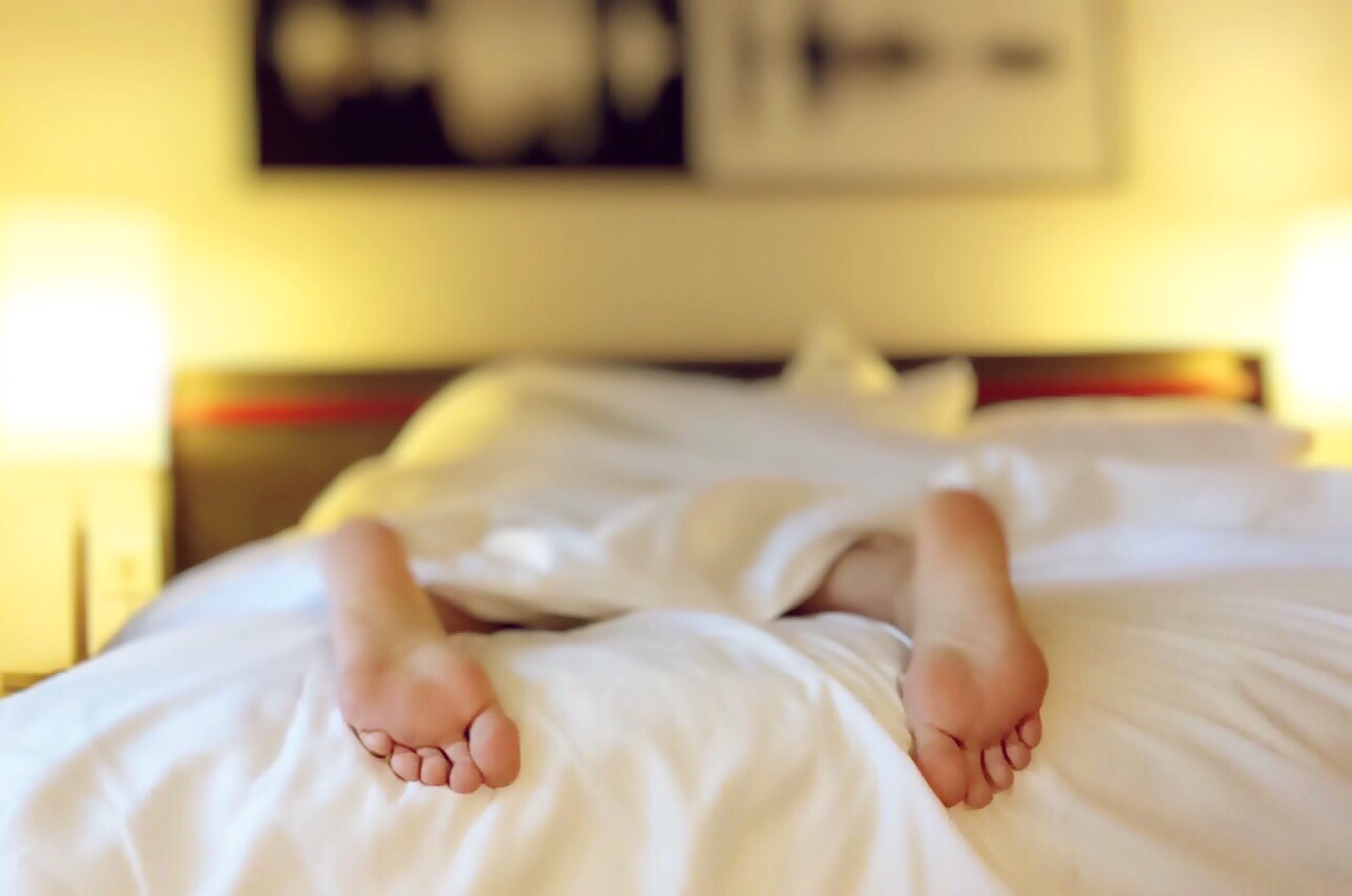 Person's feet hanging off the end of their bed in a bedroom.
