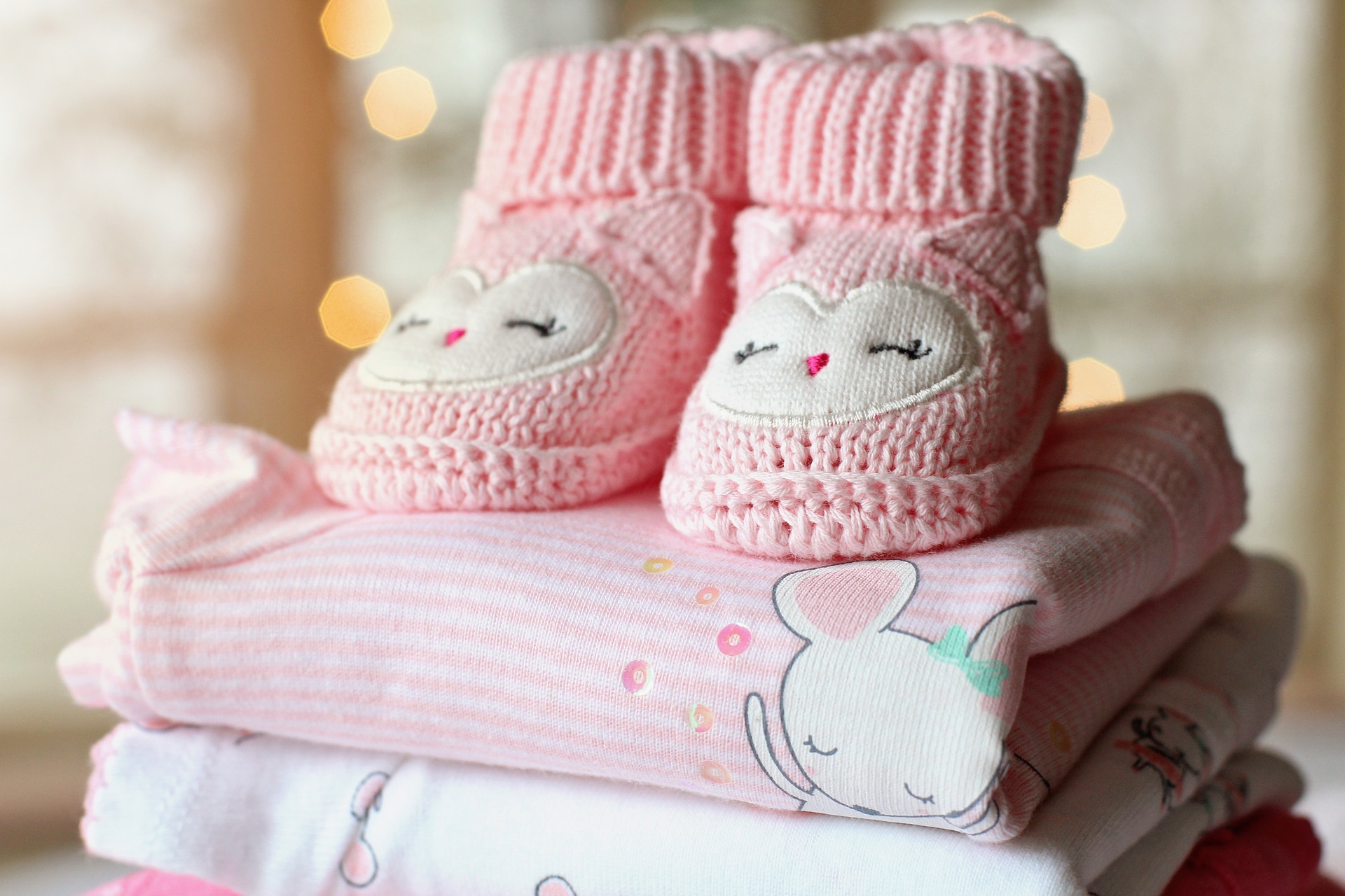 Pink baby bootie and blanket stacked in a nursery.