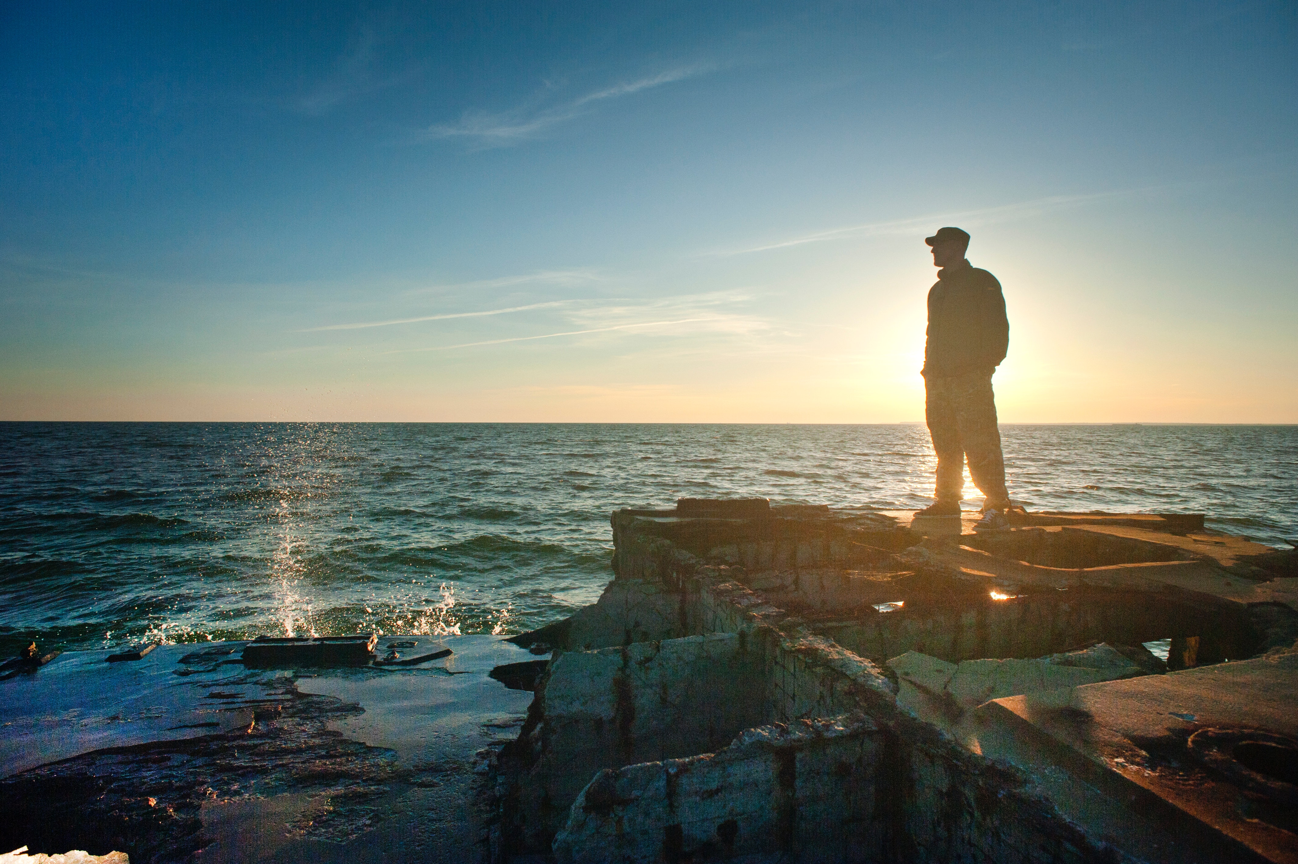 Man on a jetty looking out over the water at sunset.
