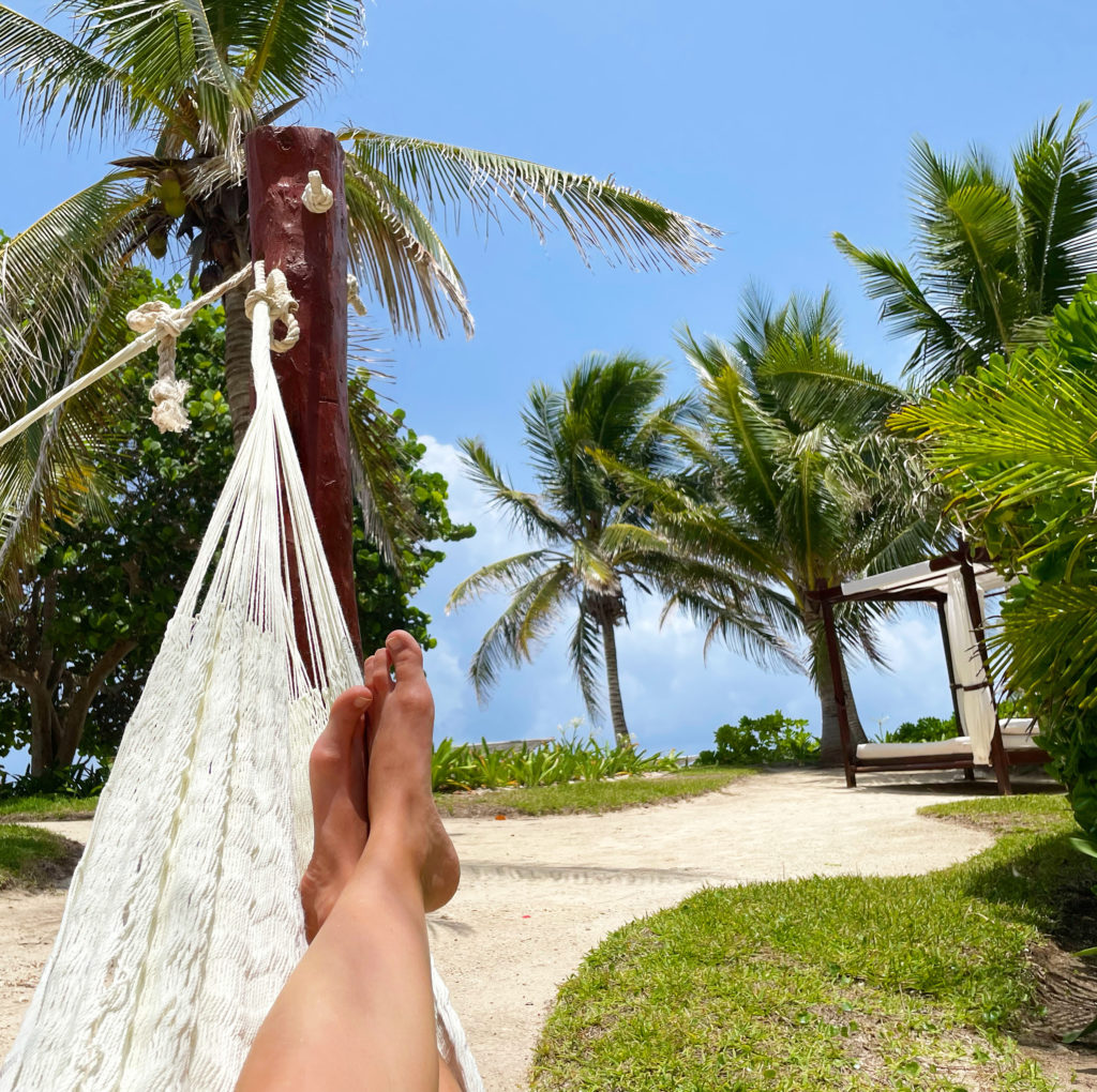 Looking out at feet in a hammock on a palm tree covered beach
