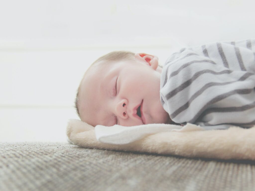 Newborn baby in comfortable pajamas sleeping on a beige blanket